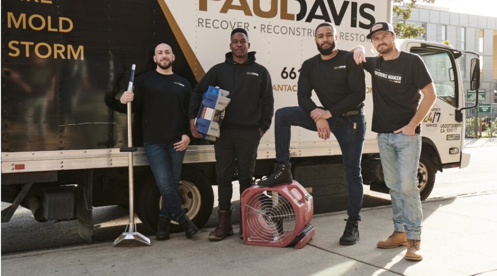 Paul Davis Restoration of Southeast MO, Carbondale & Paducah team members standing in front of a service truck with restoration equipment, including a commercial air mover and tools, ready for water, fire, and mold damage cleanup.